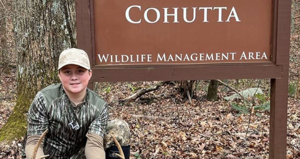 A young hunter in front of the Cohutta WMA sign.